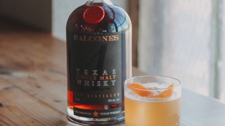A bottle of Balcones Texas 1 Single Malt Whiskey next to a whiskey sour