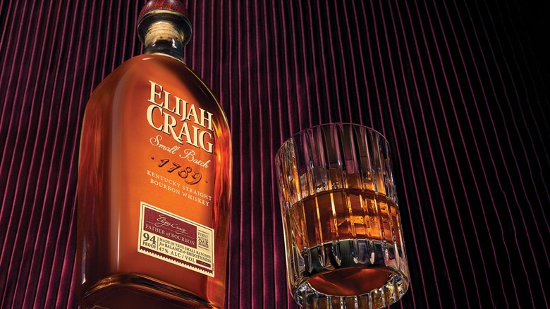 A bottle of Elijah Craig Small Batch next to a poured glass against a dark striped background