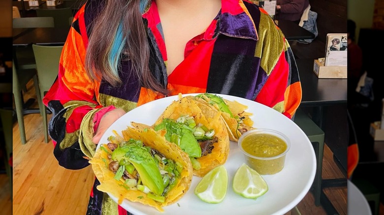 woman holding plate with tacos 