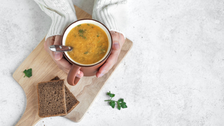 Hands holding soup mug with crackers