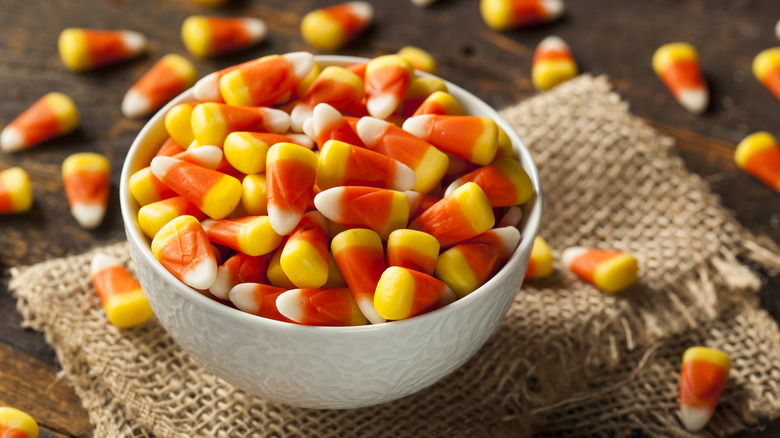 White bowl of candy corn with more candy spilled around it