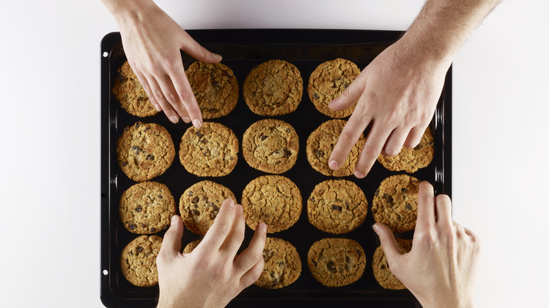 Hands grabbing cookies baking sheet