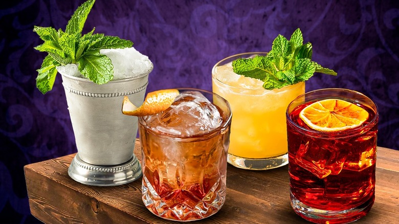 A composite image of three classic cocktails in glasses with various garnishes on a wooden counter and a purple background