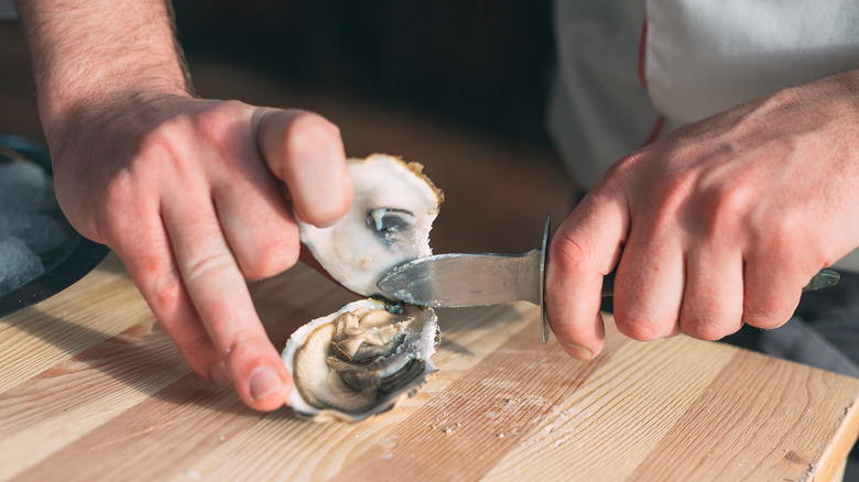 Opening oyster with knife on cutting board