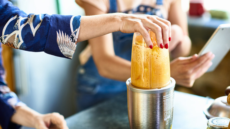 Person preparing a smoothie in a small kitchen blender