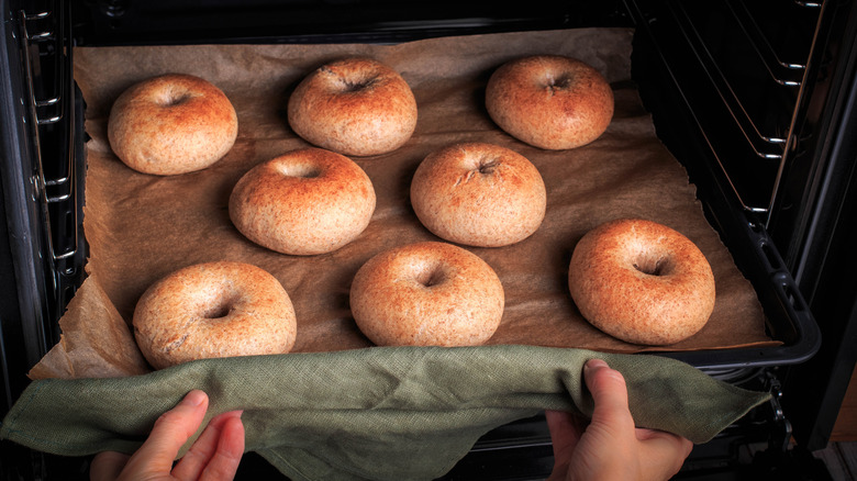 hands pulling tray of bagels from the oven