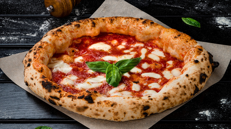 A crusty margherita pizza with fresh basil on parchment
