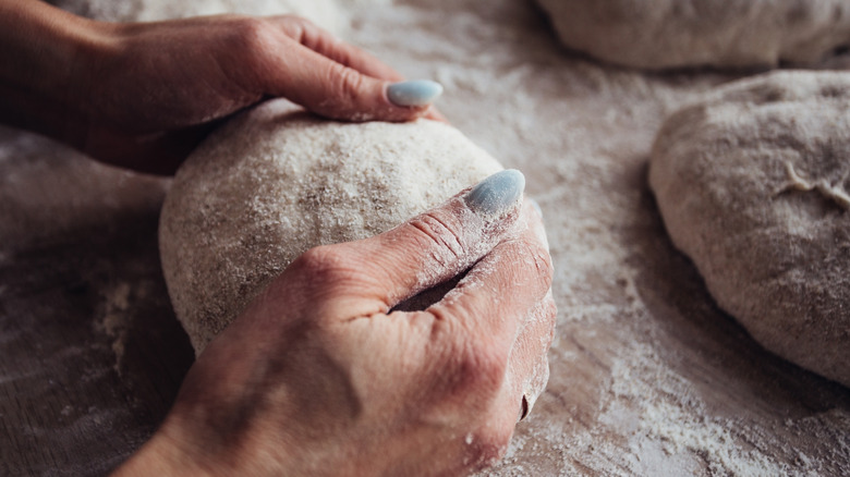 A woman shapes a ball of fresh pizza dough with flour