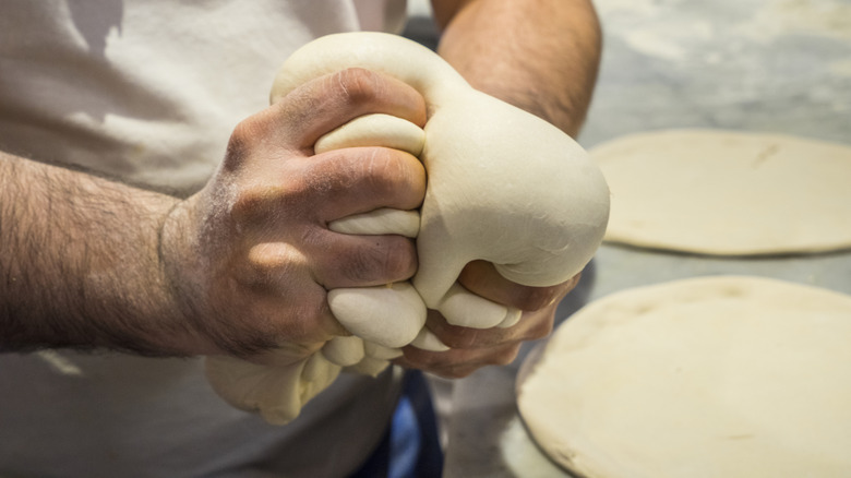A pizza chef squeezes a ball of pizza dough with his hand