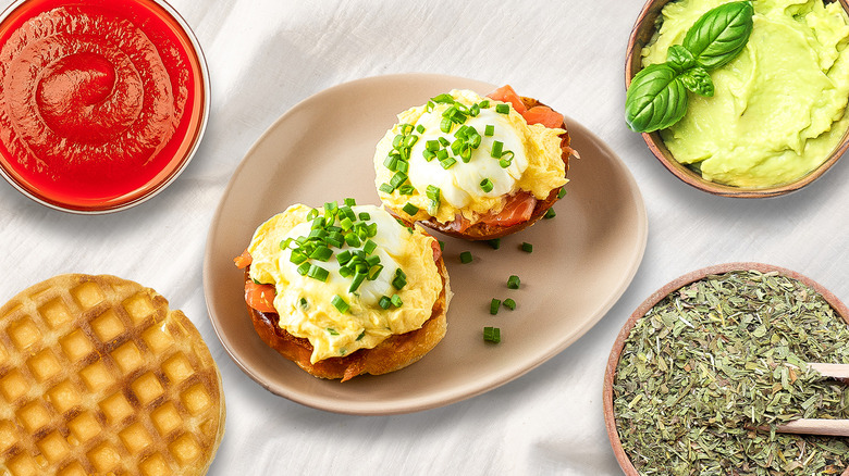 Eggs Benedict, sauce, mashed avocado, herbs, and waffle