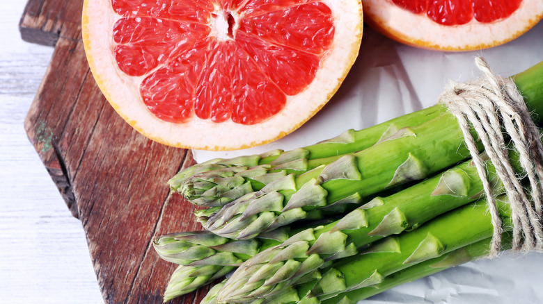 fresh bunch of asparagus and sliced grapefruit on a cutting board