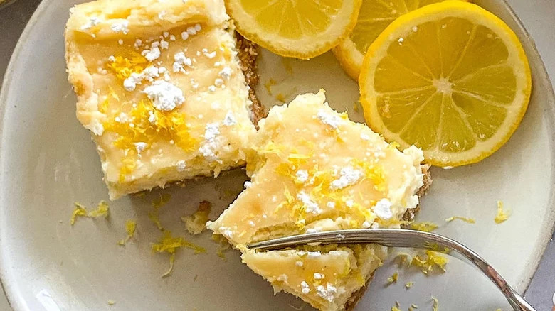 Lemon Cheesecake Bars with lemon zest, powdered sugar, and lemon slices on a plate