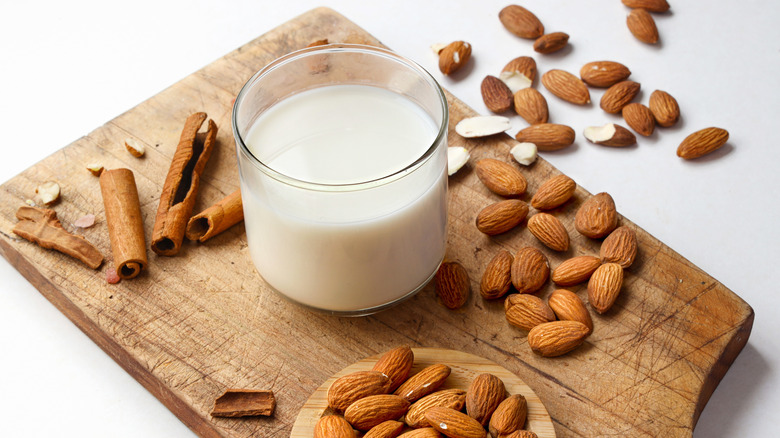 Glass of almond milk surrounded by almonds and cinnamon sticks