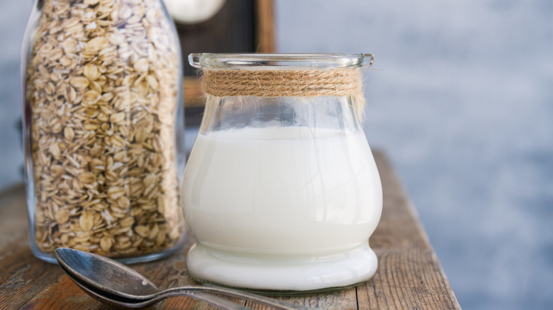 Pitcher of oat milk with spoon and bottle of oats