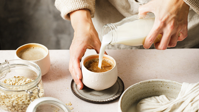 Person pouring oat milk into cup of coffee