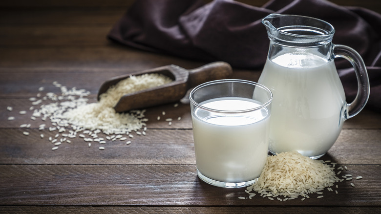 Jug and glass of rice milk surrounded by grains of rice