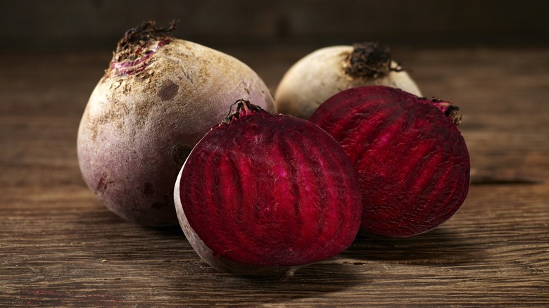 Whole and halved red beets on a wooden surface