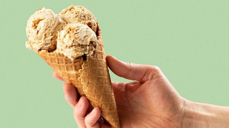 A person holds out a waffle cone with three scoops of gelato