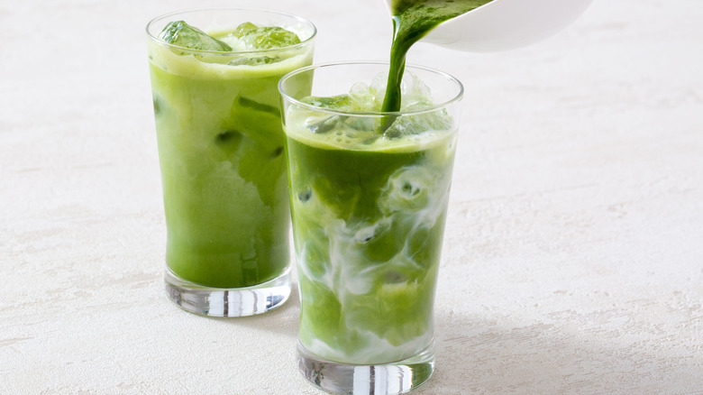 matcha pouring into two matcha lattes in tall glasses