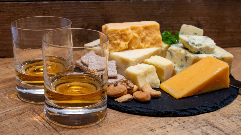 Two glasses of whisky with various plated cheeses