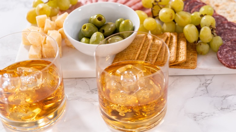 Two glasses of Scotch on the rocks with a charcuterie board