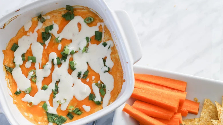 Creamy buffalo chicken dip in bowl next to carrots and chips