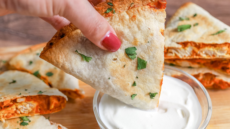 chicken tikka masala quesadilla being dipped in sour cream