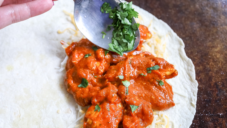 cilantro being spooned over chicken on a tortilla