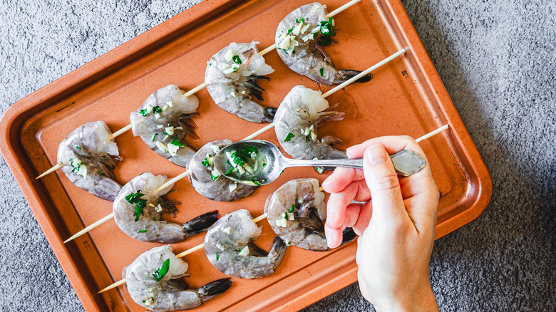 Hand spoon marinade over skewered shrimp