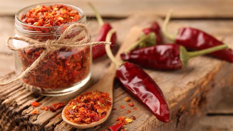 red pepper flakes in jar and spoon with whole peppers