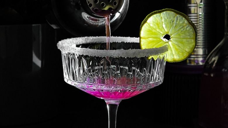 A cocktail being poured into a sugar-rimmed glass with lime