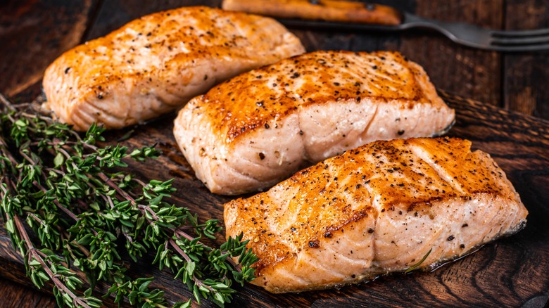 Three cooked pieces of salmon on a wooden board