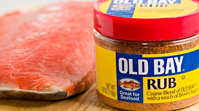 A jar of Old Bay rub next to a raw filet of salmon