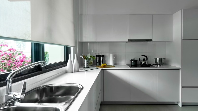 Sleek white kitchen with handless cabinets and a window behind the sink