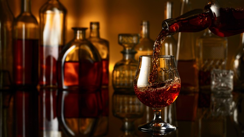 Brandy being poured into a glass in front of other bottles of liquor