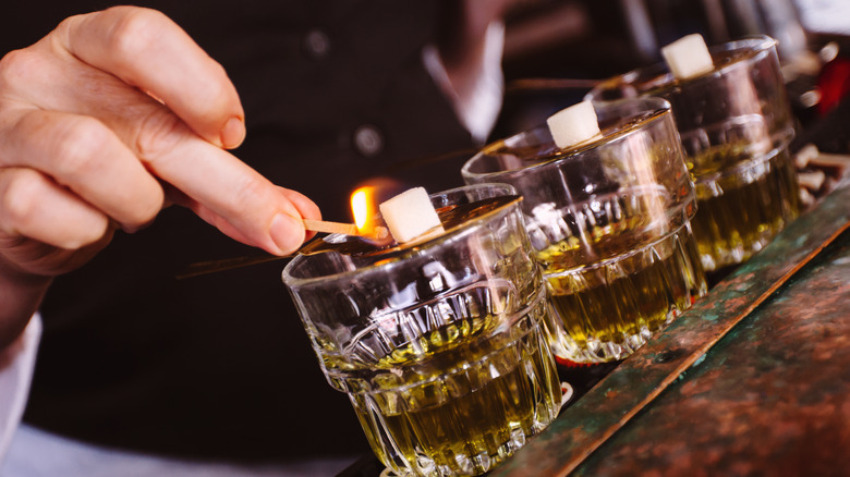 Bartender dropping flaming sugar cubes into absinthe shots