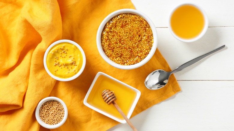 Overview of bowls of honey and mustard seeds on yellow towel