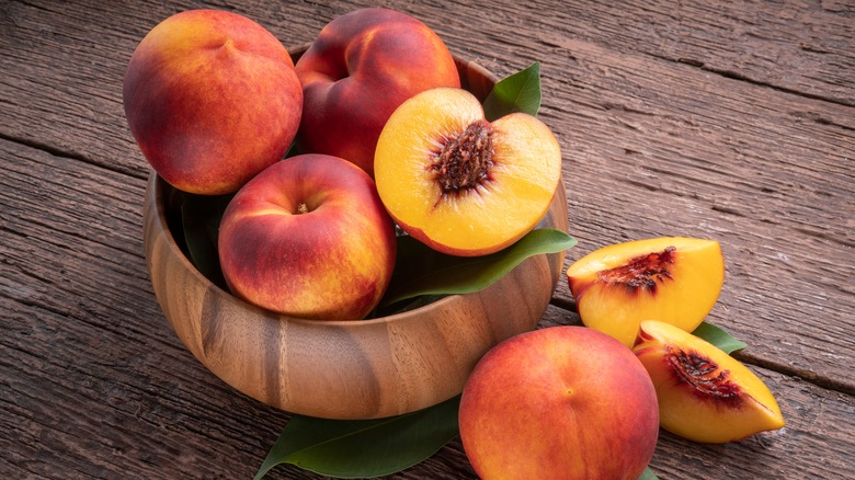 Whole and cut peaches in a wooden bowl