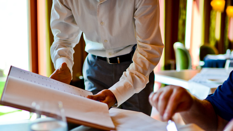 sommelier showing wine list to diner at a restaurant