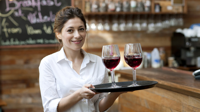 woman server carrying two glasses of red wine on a tray