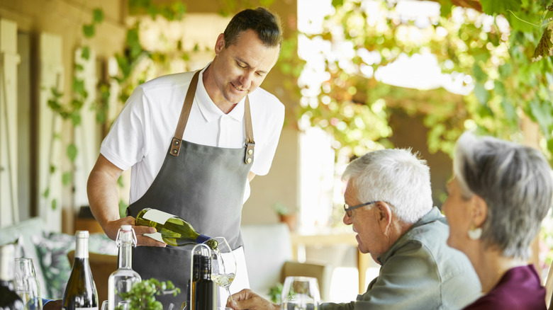 sommelier pouring a white wine for a man and woman dining at a restaurant