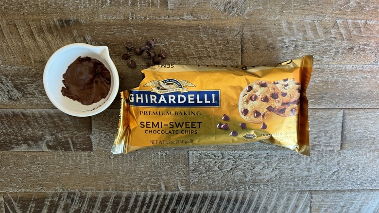 Chocolate chips spill out of a package next to a cup of melted chocolate.