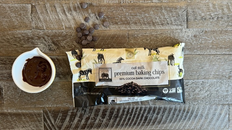 Endangered Species oat milk chocolate chips are spilling out of a bag next to a cup of chocolate.