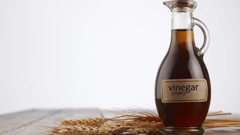 jug of malt vinegar on wooden table with wheat