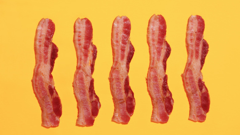 Fried strips of streaky bacon slices on yellow background