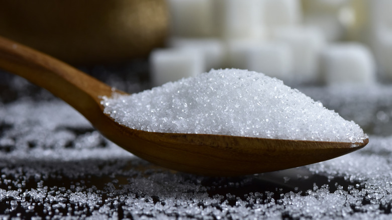 Closeup of a wooden spoon filled with white sugar