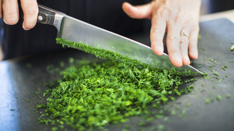 Closeup of a person chopping fresh parsely with a knife on a dark cutting board