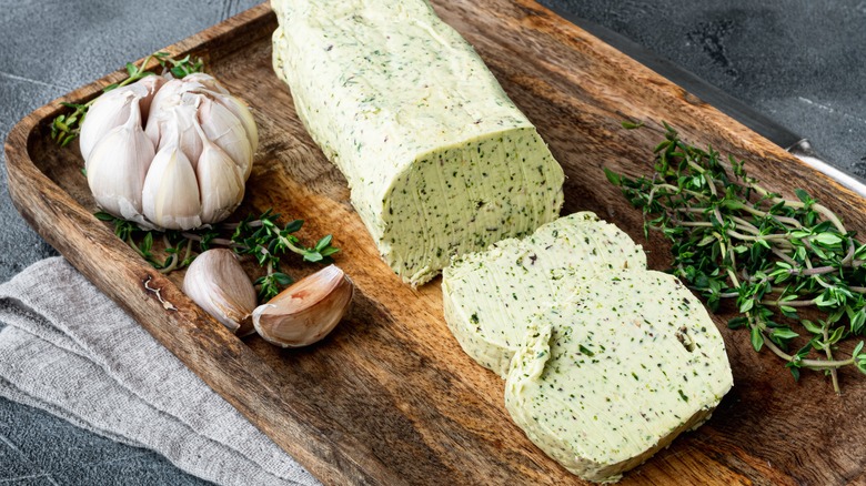 Herbal compound butter on a wooden tray with garlic cloves and thyme sprigs