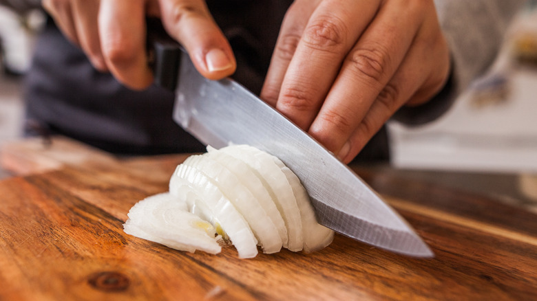 Closeup of a person slicing an onion on a wooden board