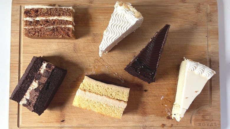 Six slices of various Costco cakes on wooden cutting board